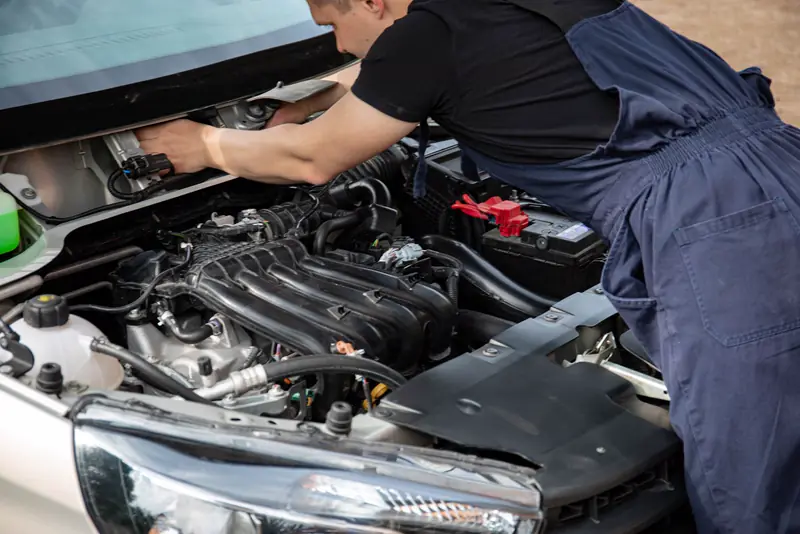 Mehaničar u radnom kombinezonu popravlja motor ispod otvorene haube automobila